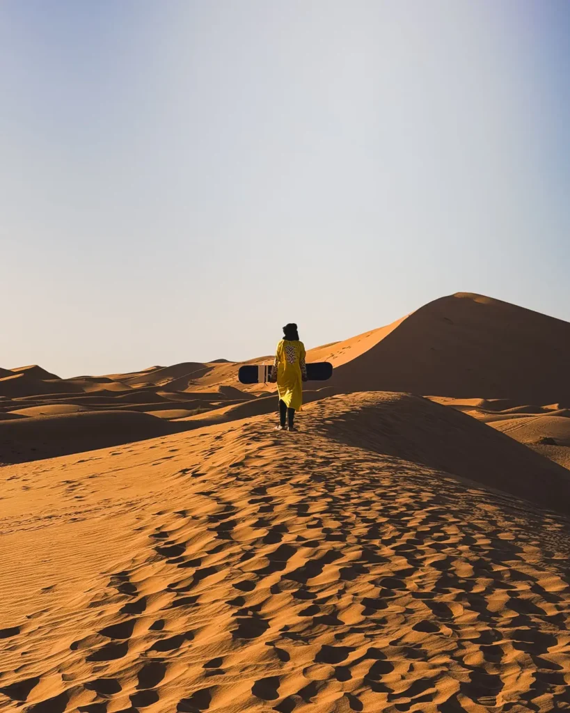 Carrying a sandboard up a desert dune at sunset