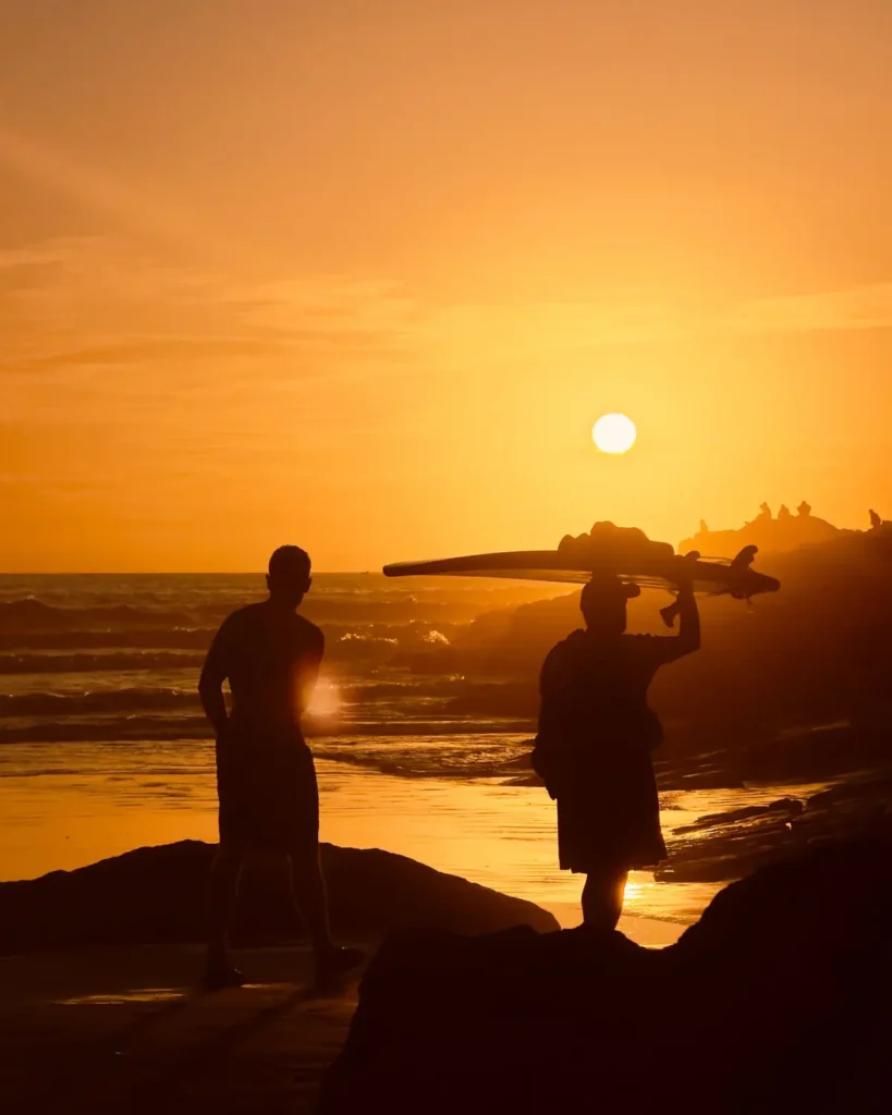 Surfers carrying their boards on Taghazout beach at sunset