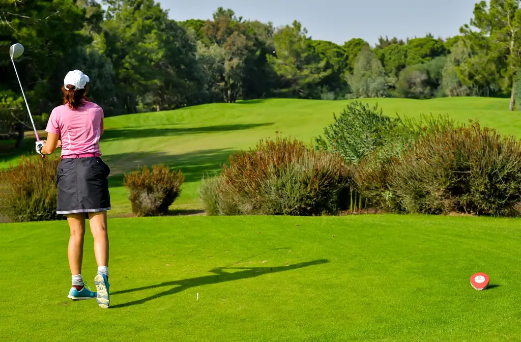 Golfer playing a tee shot on a green fairway lined with shrubs