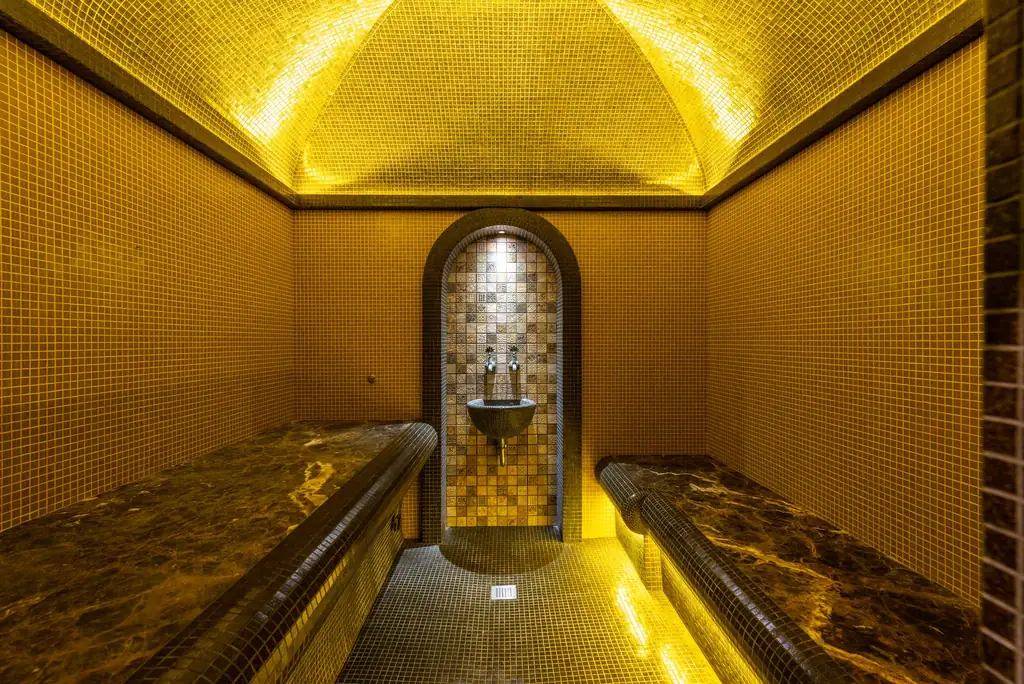 Mosaic steam room with marble benches and warm lighting, typical of a hammam spa