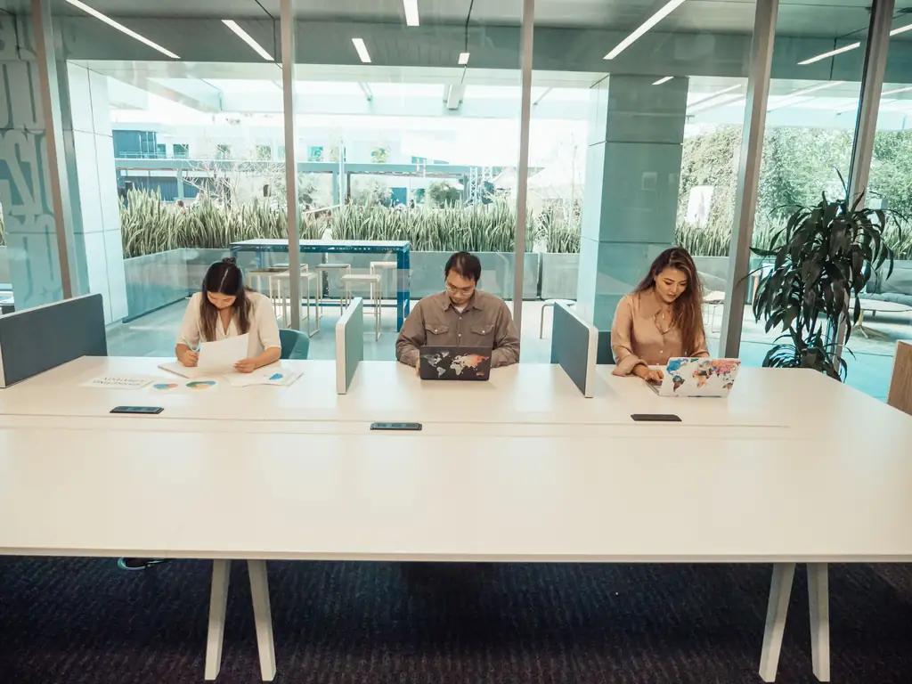 Three professionals working on laptops at a shared desk in a coworking space