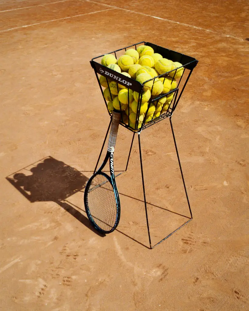 Basket of tennis balls and a racket on a clay court, ready for a coaching session